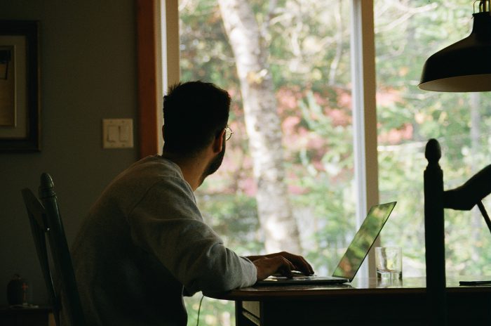 Un homme assis devant son ordinateur regarde par la fenêtre.